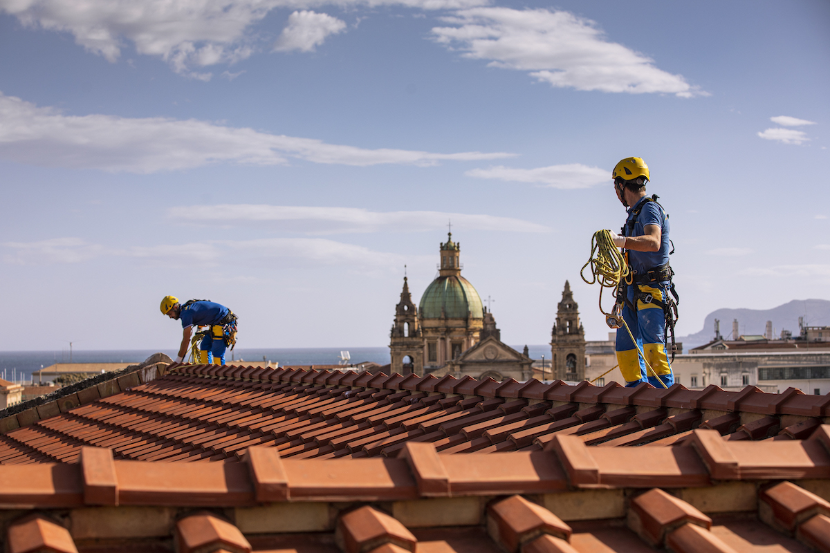 Trabajadores durante una operación con cuerdas para crear una envoltura térmica en el techo de Palermo