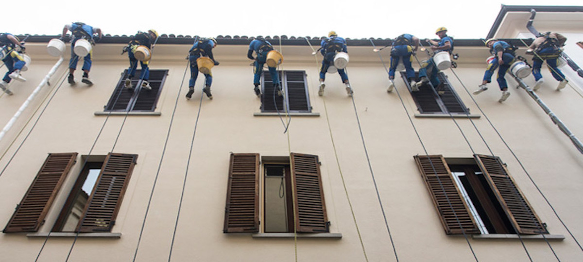 Muchos trabajadores desde atrás intentan sujetar una cuerda con la fachada de un edificio al fondo.