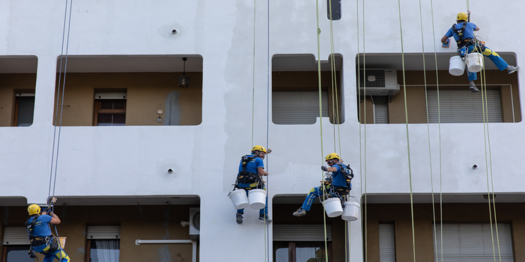 Operarios en cuerdas de espaldas impermeabilizando la fachada de un edificio