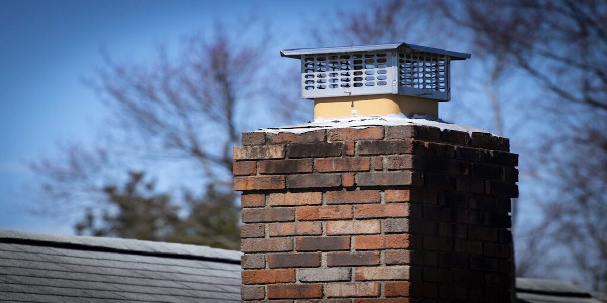 Chimenea para estufa de leña de ladrillo, que sobresale del techo de un edificio conforme a la normativa.