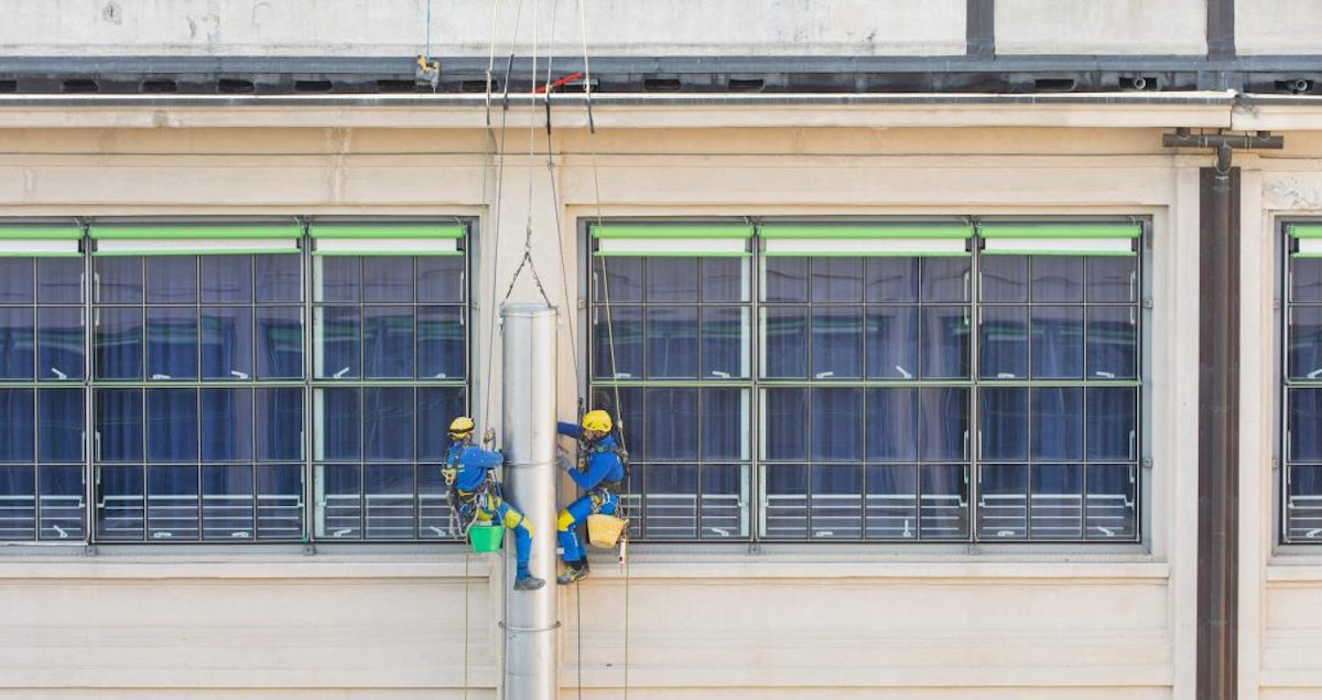 Trabajadores de Acrobatica suspendidos con cuerdas mientras instalan una chimenea para estufa de leña en un edificio, de acuerdo con la normativa de seguridad.