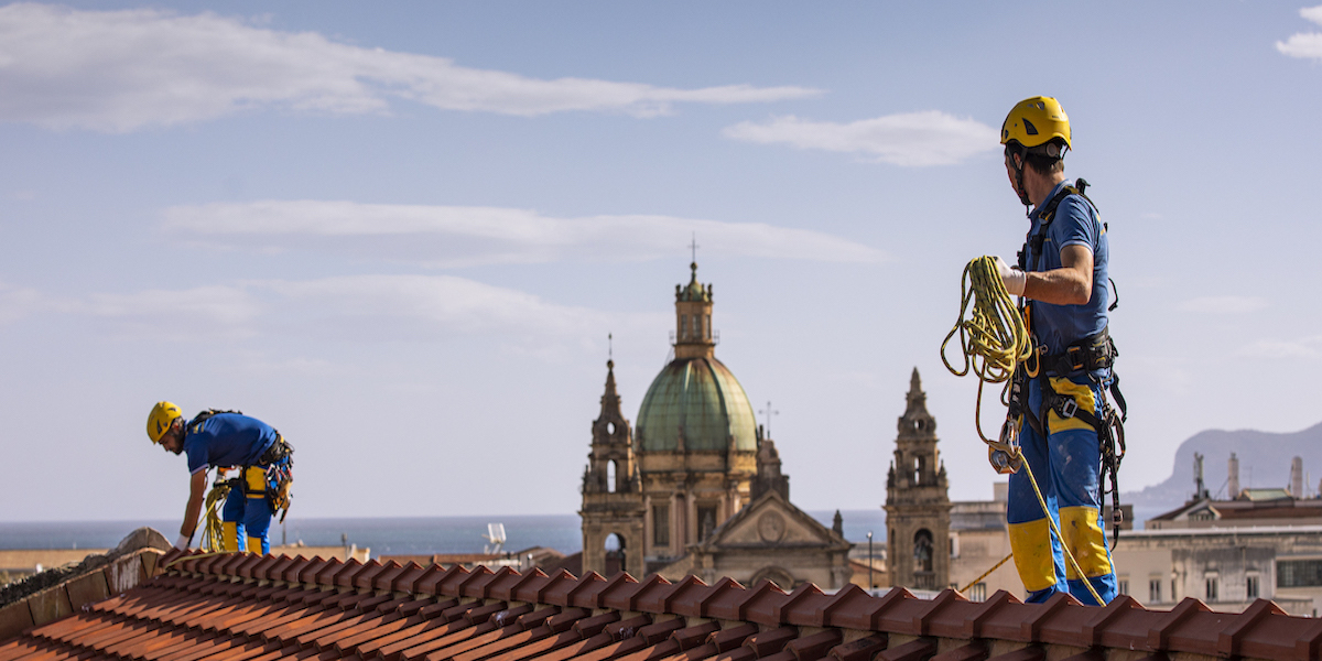 Dos operarios de Acrobatica trabajan en el techo de un edificio en Florencia instalando aislamiento térmico exterior, con vista panorámica de la ciudad al fondo