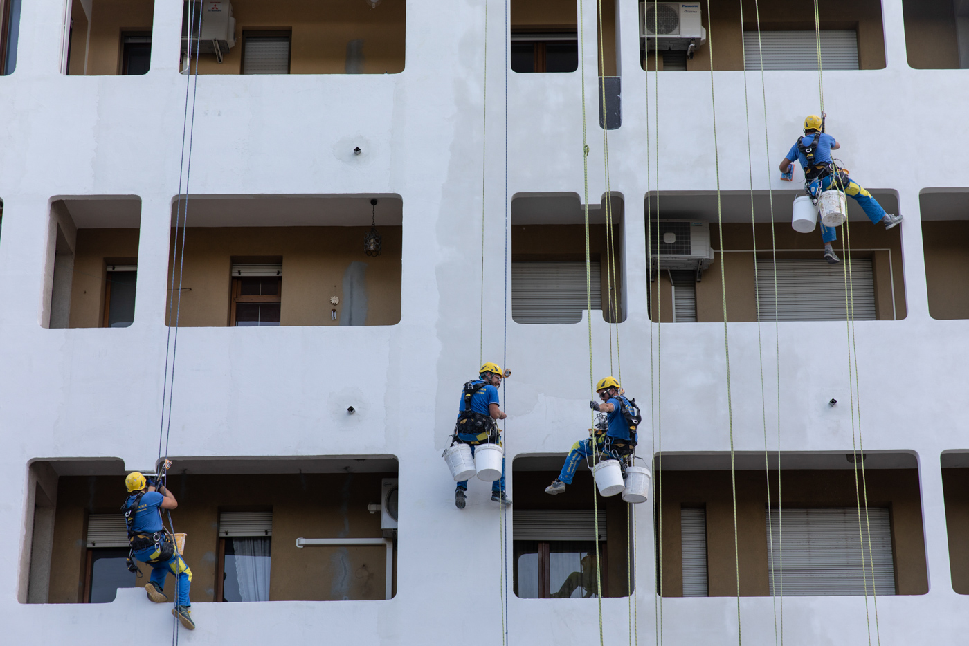 Pintores profesionales aplicando pintura a la fachada de una casa con rodillos y andamios.