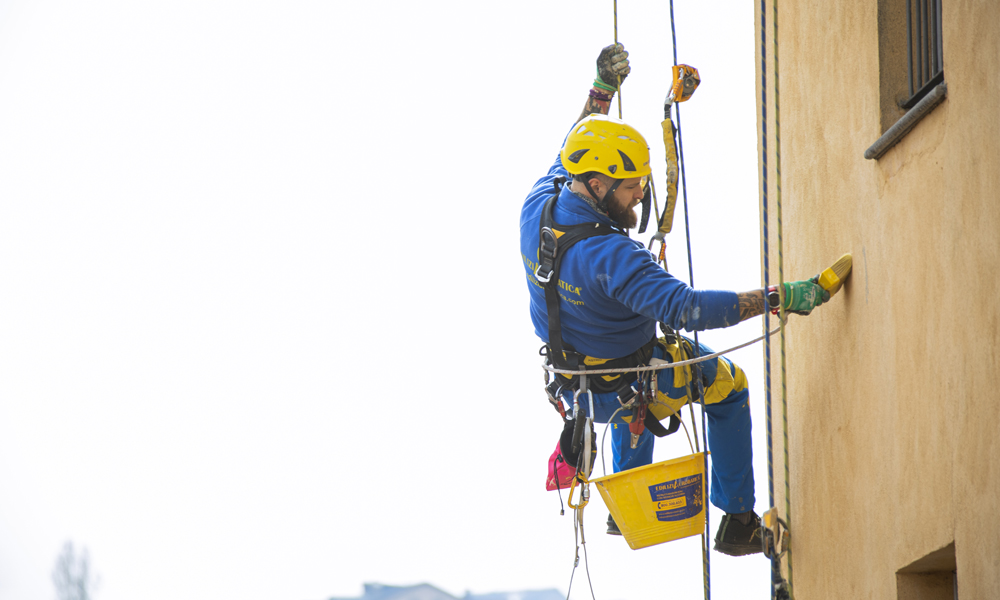 Trabajadores colgados con cuerdas mientras pintan la fachada de un edificio alto.